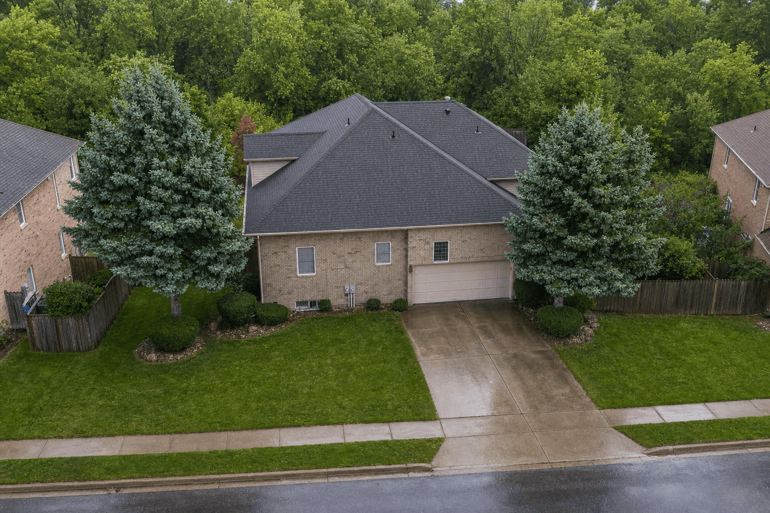 Aerial view of a brick home with a dark shingle roof and a single-car garage