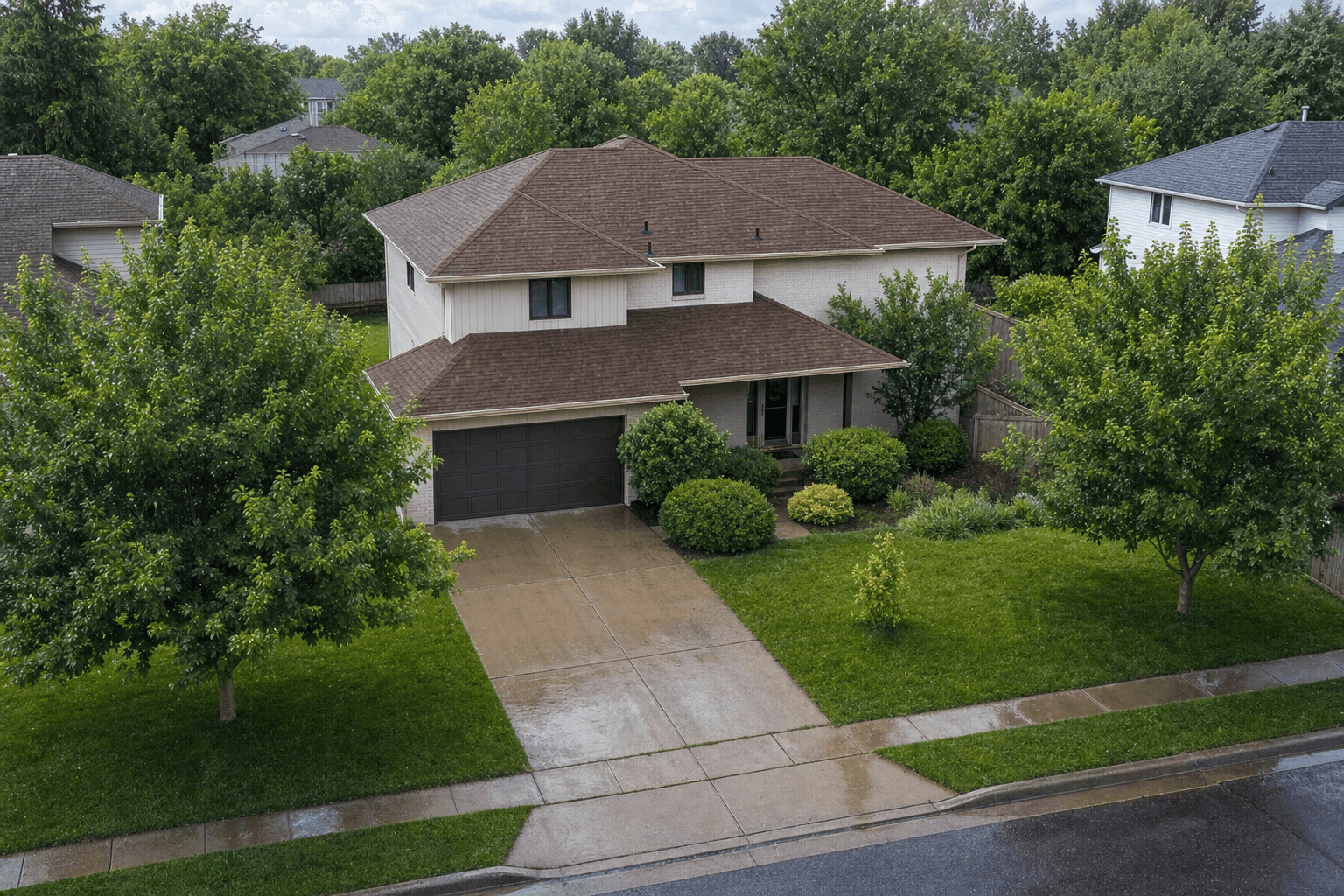 Aerial view of a two-story home with a brown shingle roof, framed by mature trees