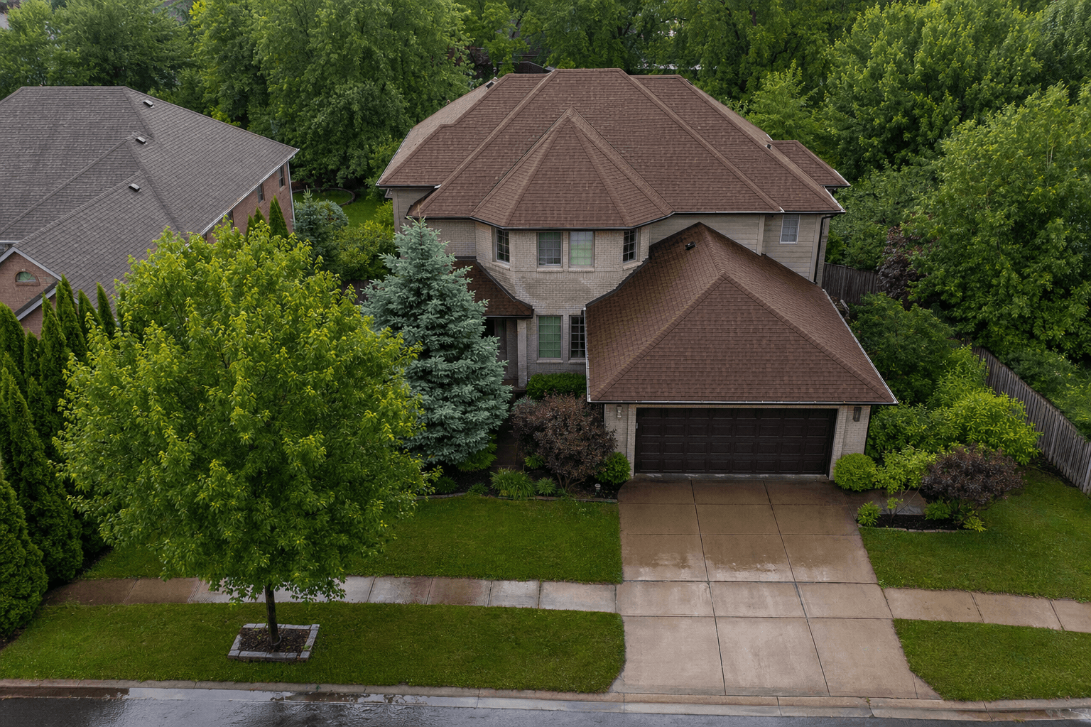 Aerial view of a large two-story home with a brown hip roof and a long driveway