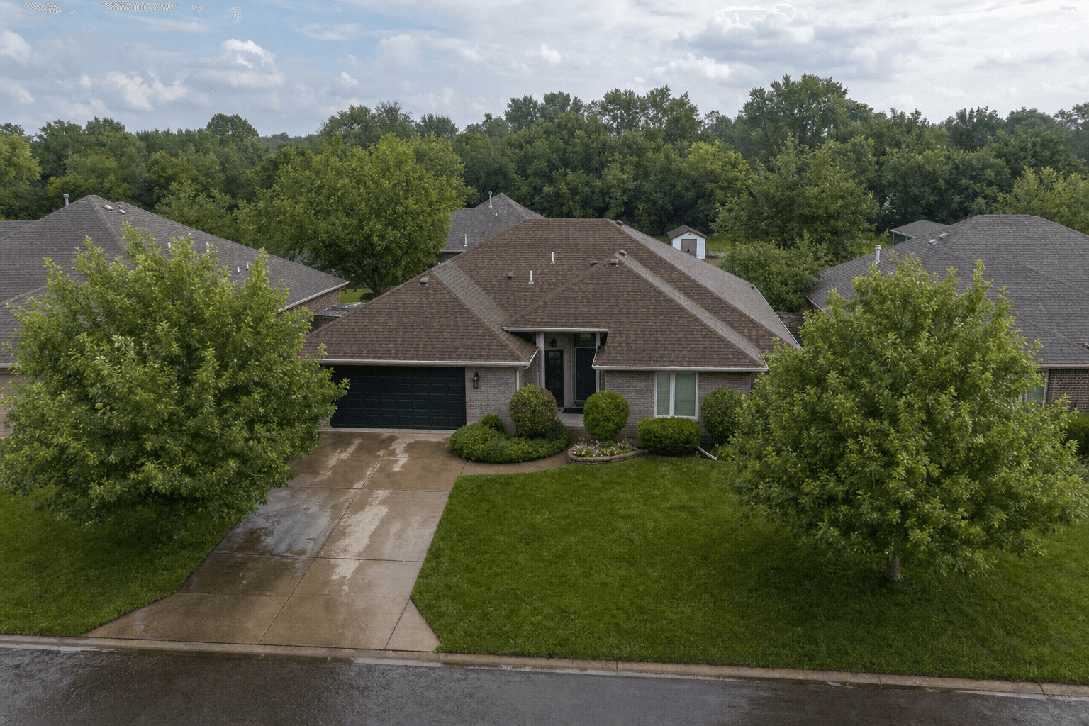 Aerial view of a single-story brick ranch home with a brown shingle roof